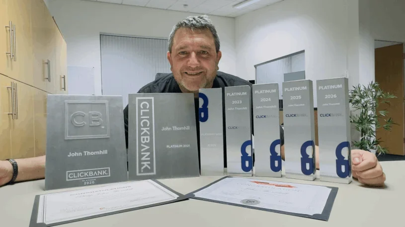 A man leaning on a table behind a row of plaques engraved ClickBank Platinum with the name John Thornhill (unverified)